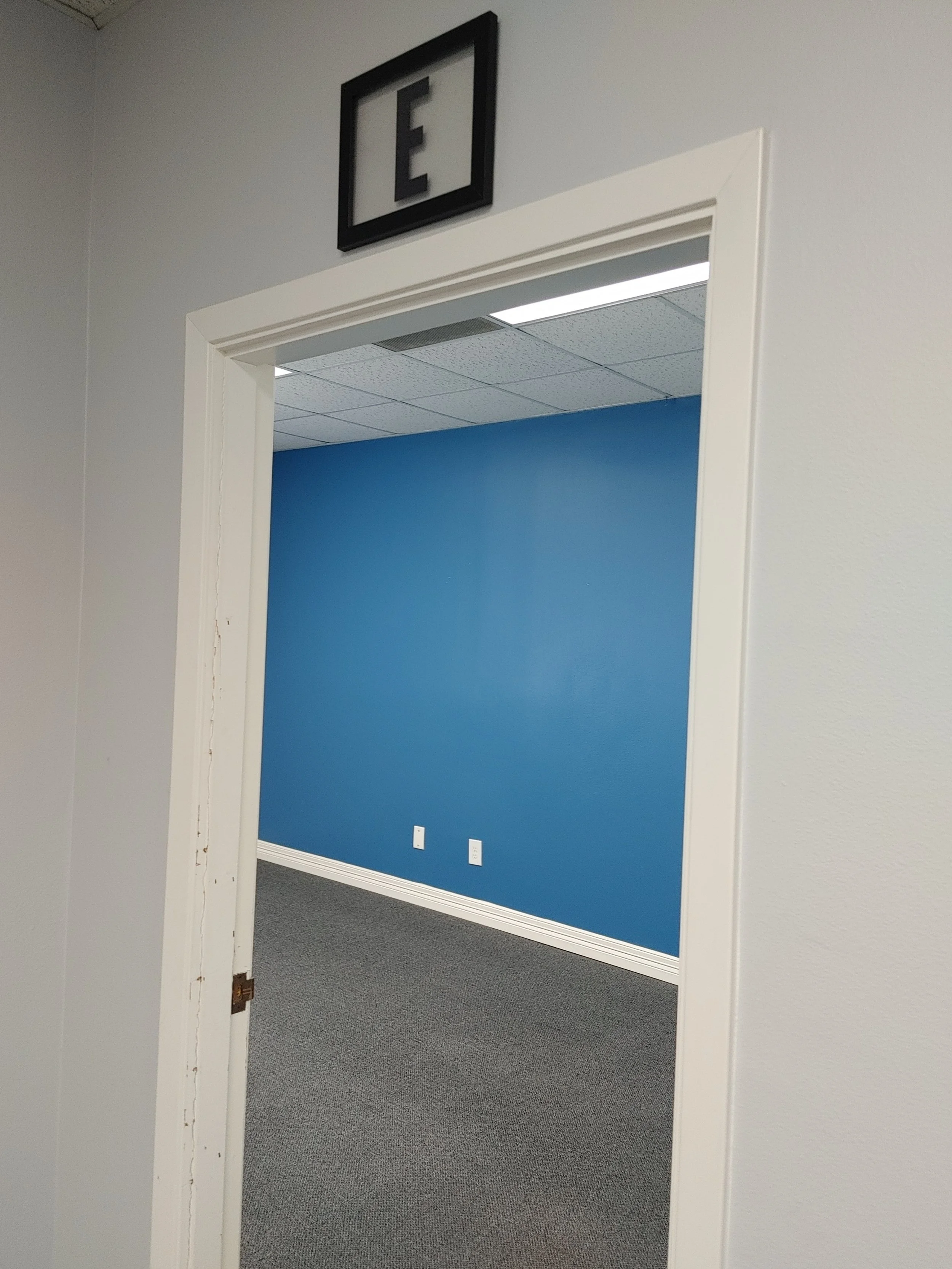 Interior view of an office space with a blue accent wall, electrical outlets, and a ceiling with fluorescent lighting.