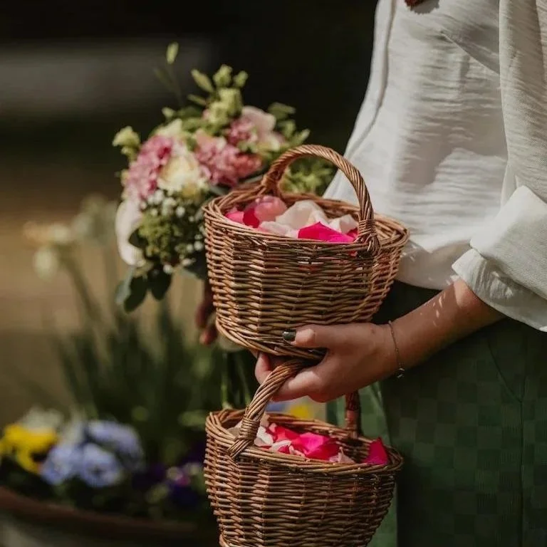 Persoon houdt een mand met rozenblaadjes, met bloemen op de achtergrond.