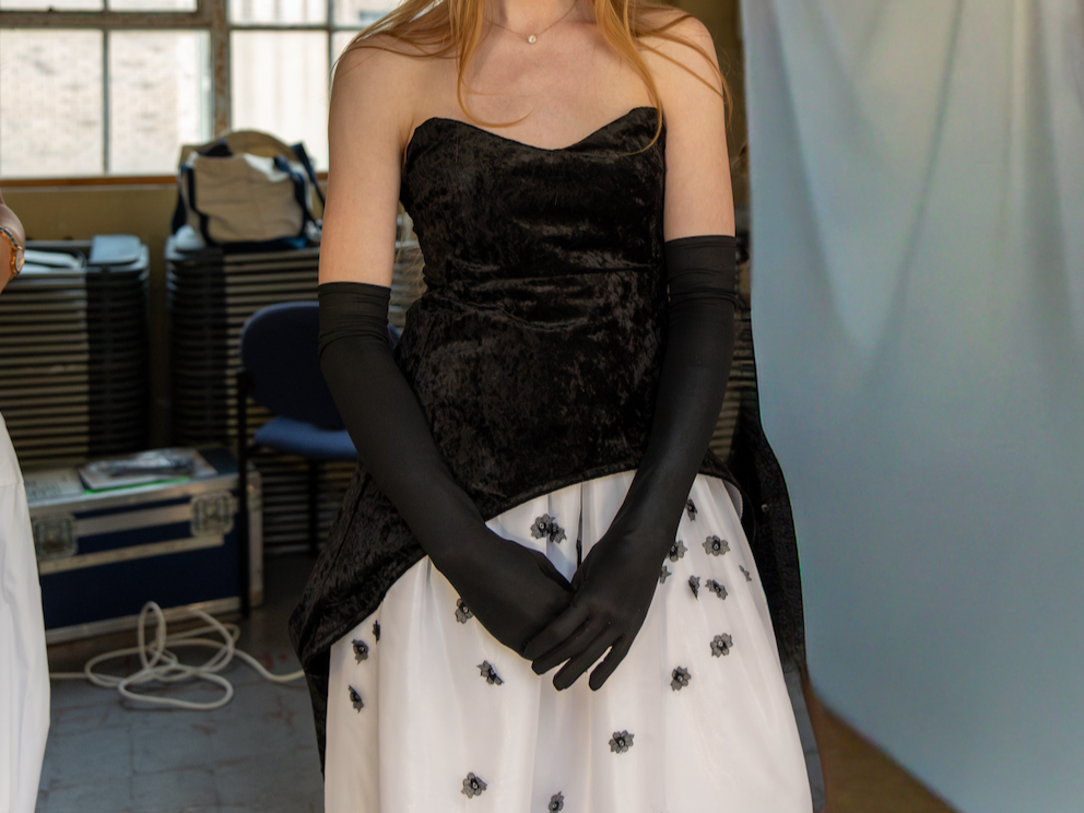 A woman wearing a black strapless dress, black gloves, and a white tulle skirt with black floral embellishments.
