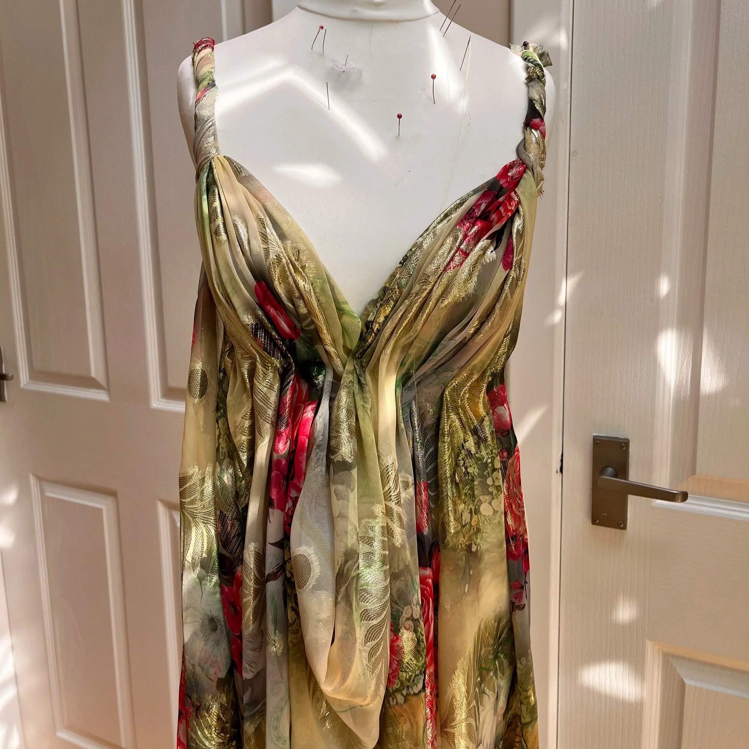 A dress on a mannequin with a floral and gold pattern, displayed in front of white paneled doors.