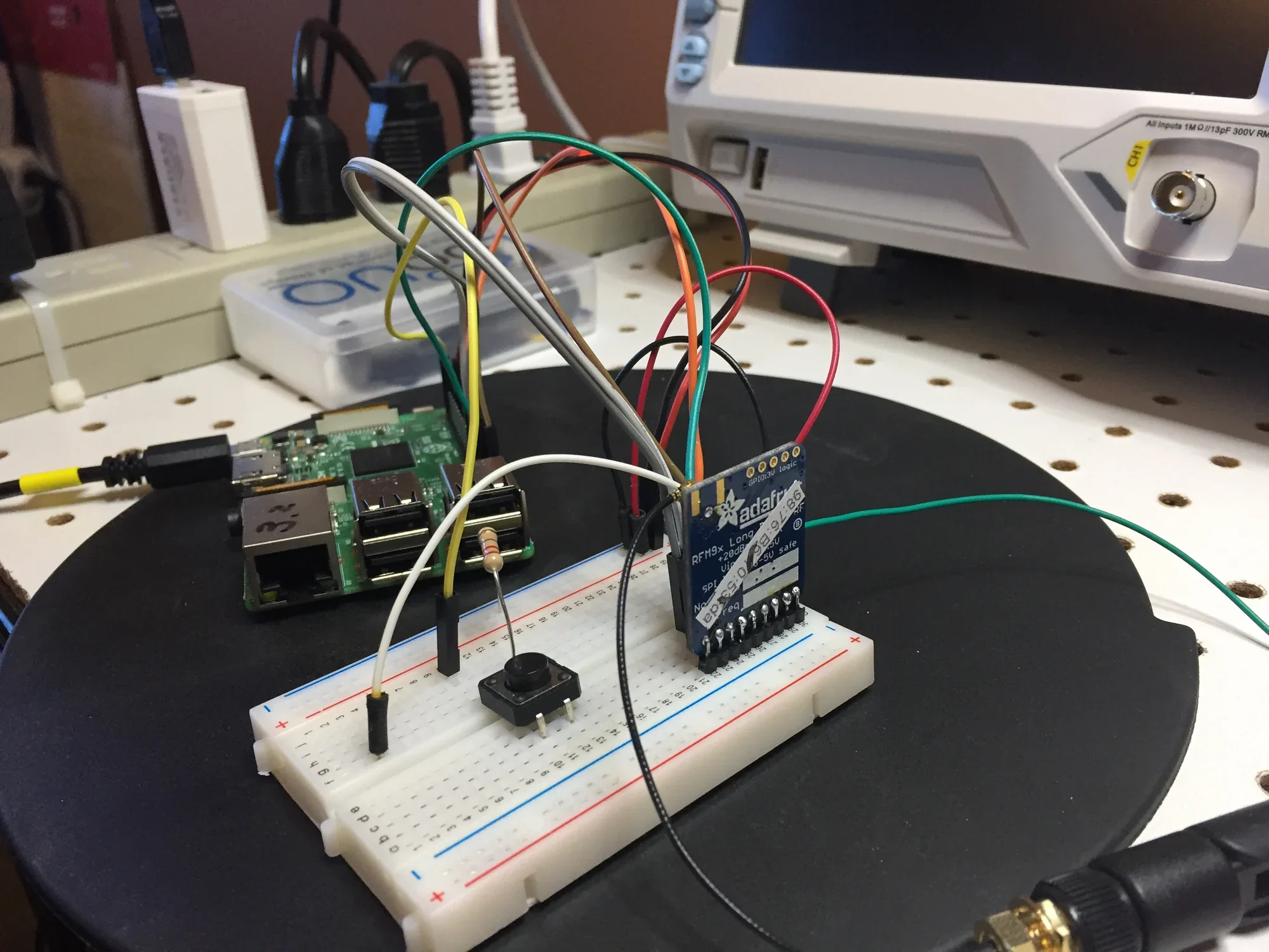 A breadboard with an Raspberry Pi microcontroller, connected wires, a small button switch, and a relay module, on a black circular surface.