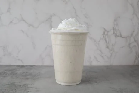 A cup of vanilla milkshake topped with whipped cream against a marble background.