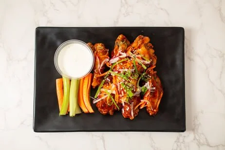 Buffalo chicken wings with ranch dip and celery and carrot sticks on a black rectangular plate