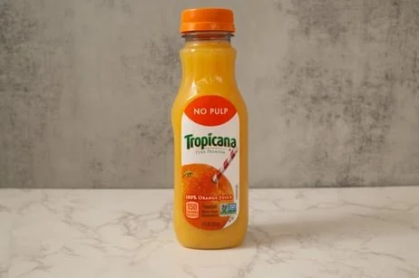 A bottle of Tropicana Pure Premium orange juice with no pulp on a marble surface against a concrete wall background.