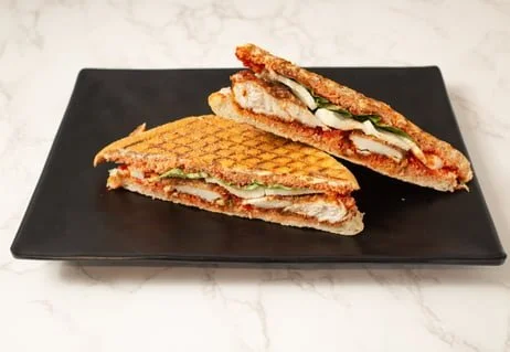 Grilled chicken sandwich with lettuce and mayonnaise, cut in half and served on a black rectangular plate.