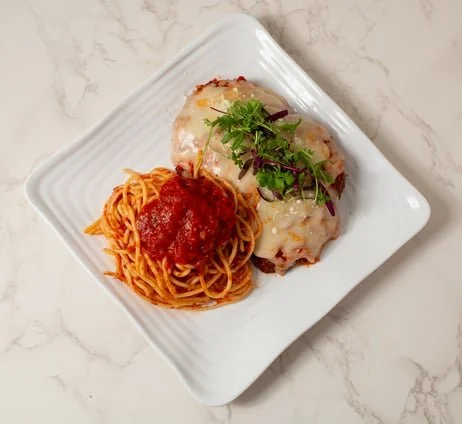 Plate with spaghetti topped with marinara sauce and two baked chicken breasts garnished with chopped herbs and greens
