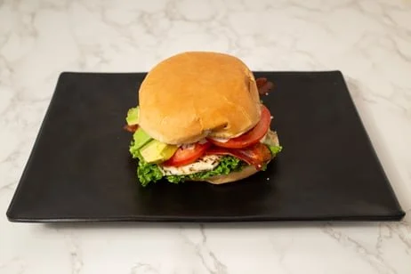A sandwich with lettuce, tomato, bacon, and other ingredients on a black rectangular plate.