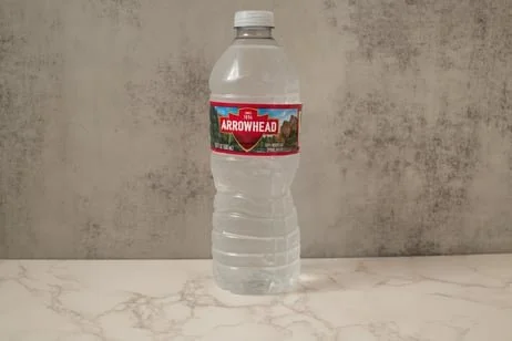 A plastic bottle of Arrowhead water on a marble surface against a concrete wall background.