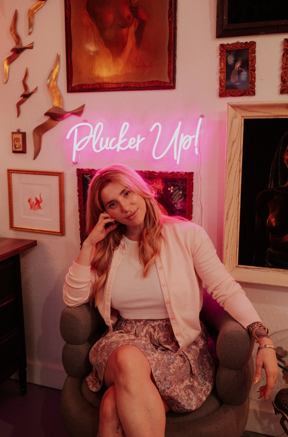Waxing studio team member seated beneath a pink neon Plucker Up sign