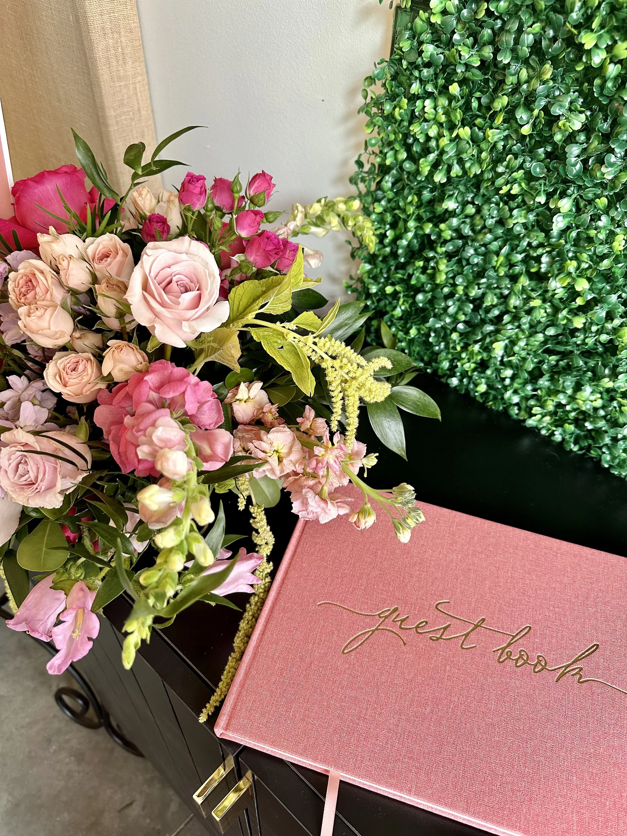 Colorful floral arrangement with pink, peach, and white roses, and pink hydrangeas, next to a pink book with gold lettering on a black table