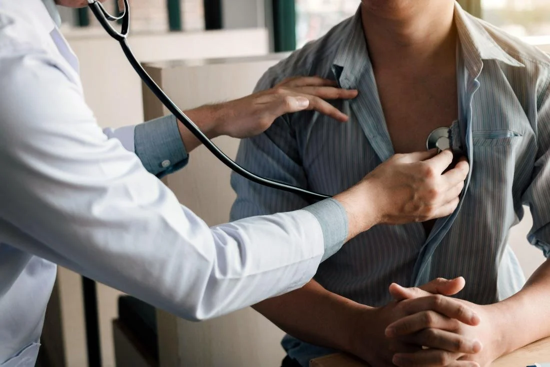 Doctor using a stethoscope on a patient's chest during a medical exam.
