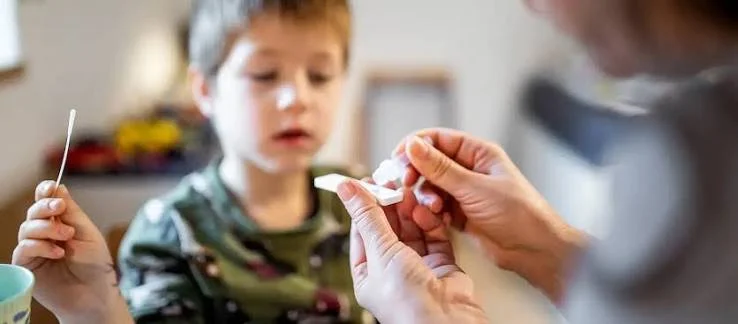 A person holding a cotton swab near a child's mouth during a medical examination in a home setting.