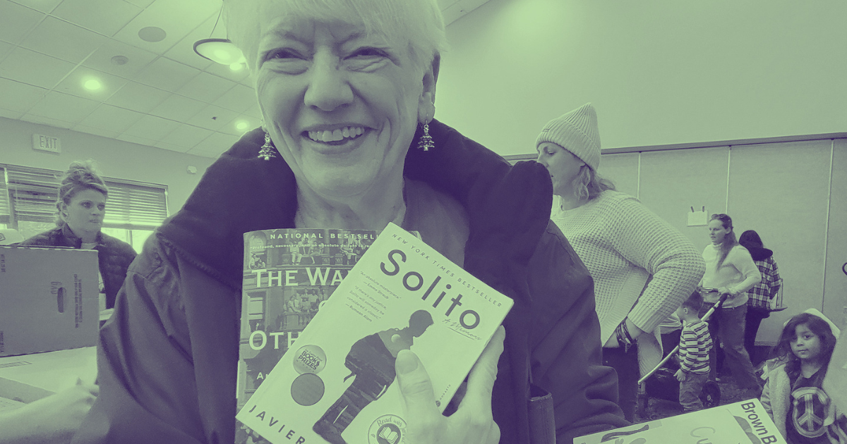 Woman smiling, holding a copy of the book "Solito" by Javier in a busy indoor setting with children and adults.