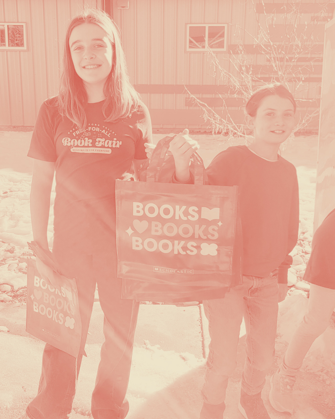 Two young girls holding Scholastic book bags outside on a snowy day, smiling at the camera.