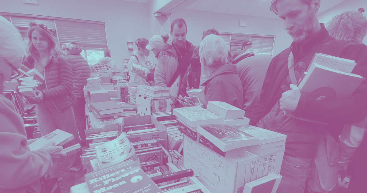 People browsing and purchasing books at a busy indoor book sale or bookstore.