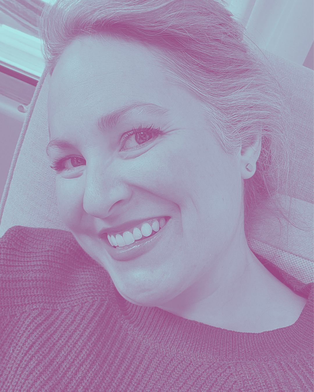 Close-up of a young woman smiling on a sofa, lying down by a window.