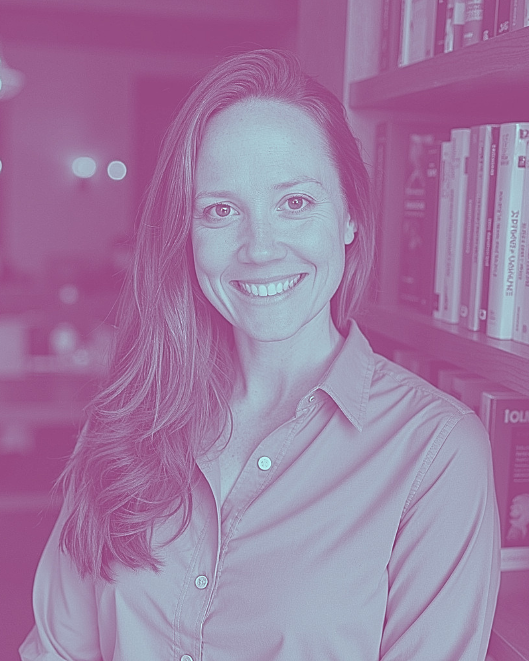 A woman with long hair smiling, standing in front of a bookshelf filled with books.
