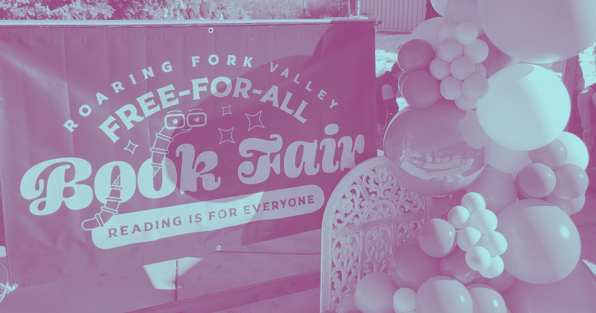 A banner promoting a book fair with the phrase 'Roaring Fork Valley Free-For-All Book Fair, Reading is for Everyone,' next to a decorative balloon arrangement.