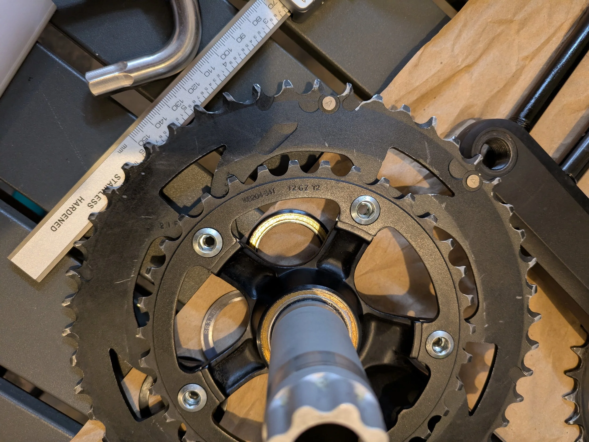 Close-up of a bicycle gear crankset with multiple chainrings and a part of a caliper brake system on a workbench.