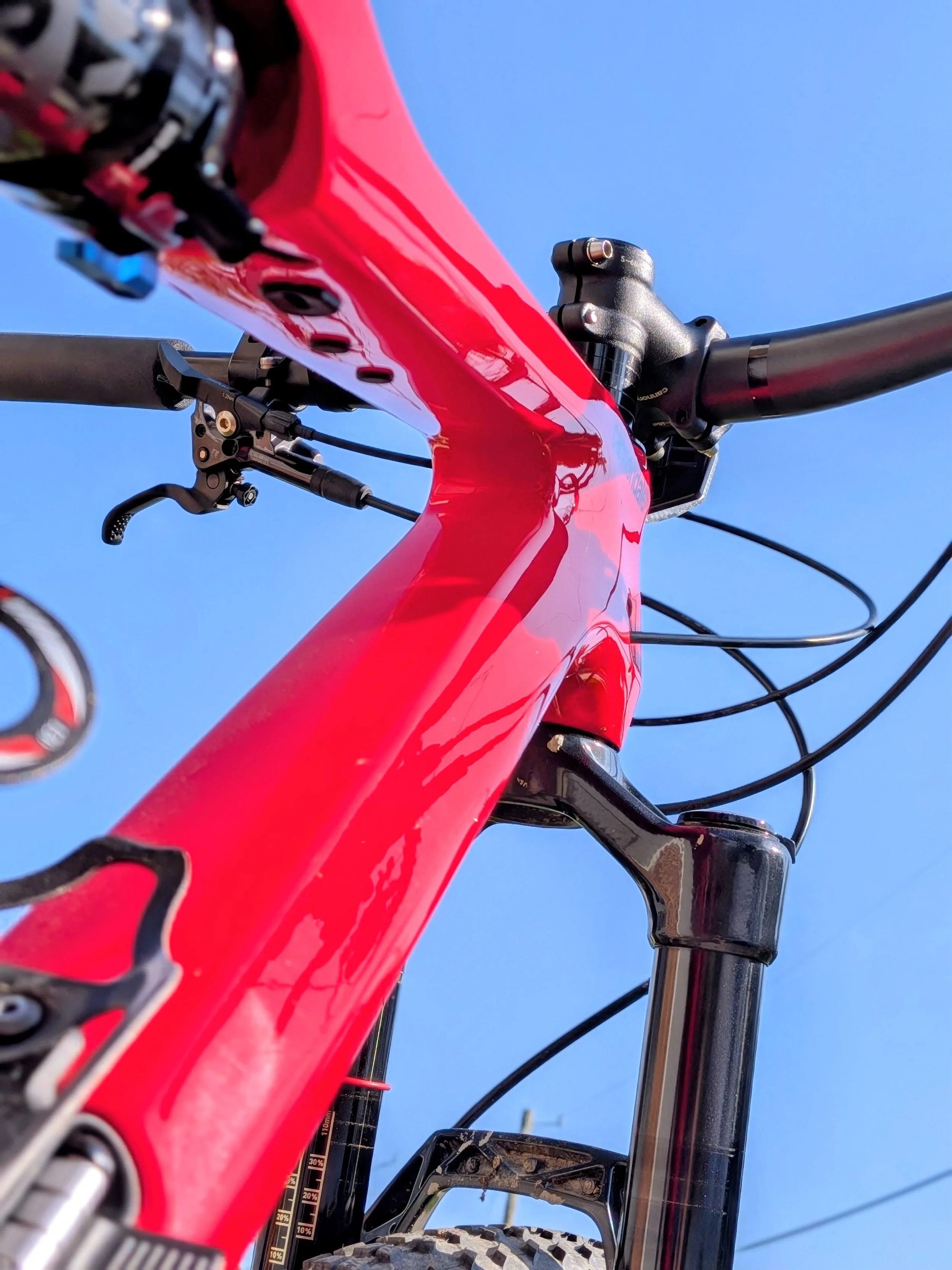 Close-up view of a red mountain bike's front suspension fork, handlebars, and part of the tire, with a clear blue sky in the background.