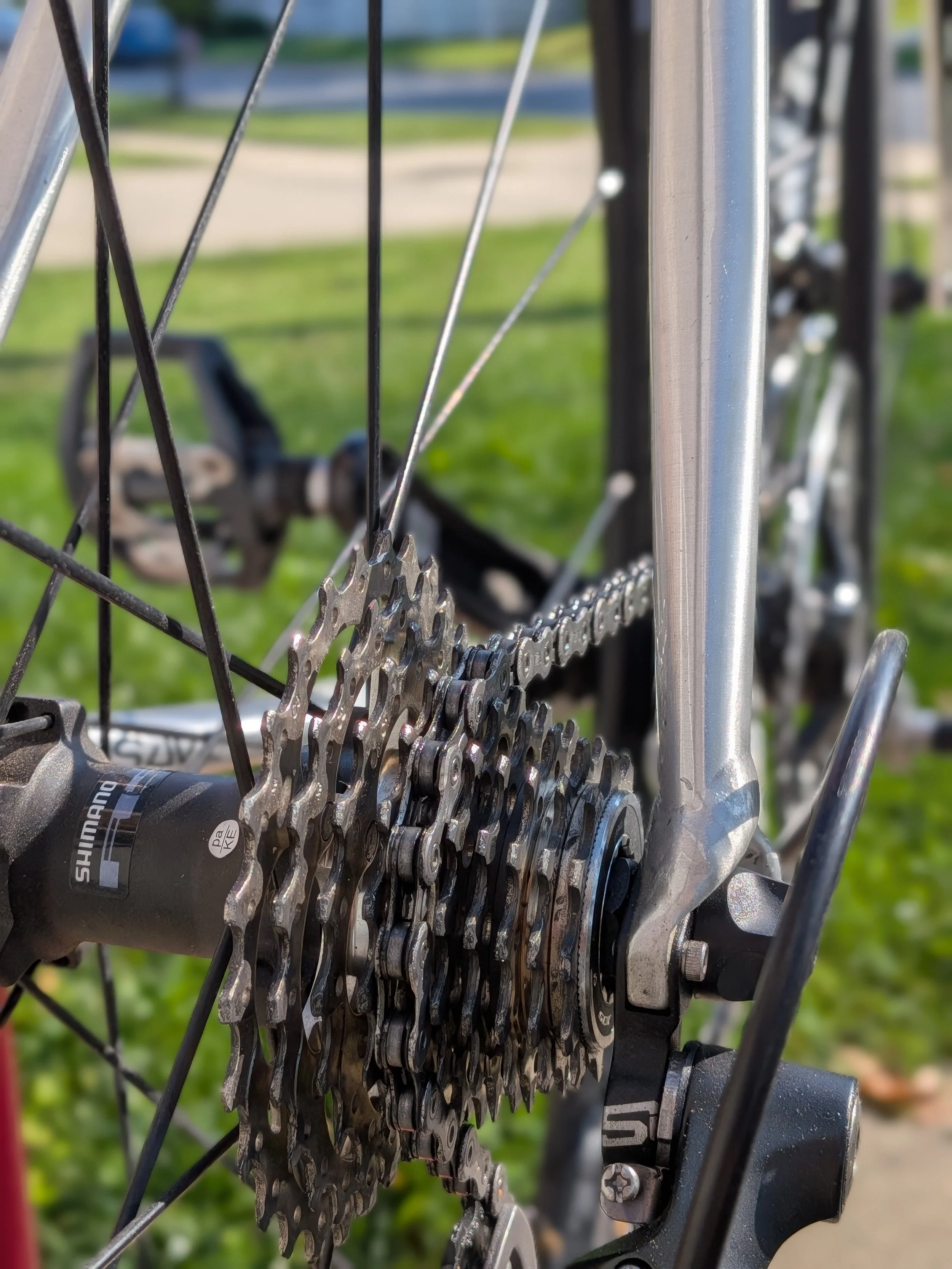 Close-up of a bicycle's rear gear cassette and chain, with a blurred green and yellow background.
