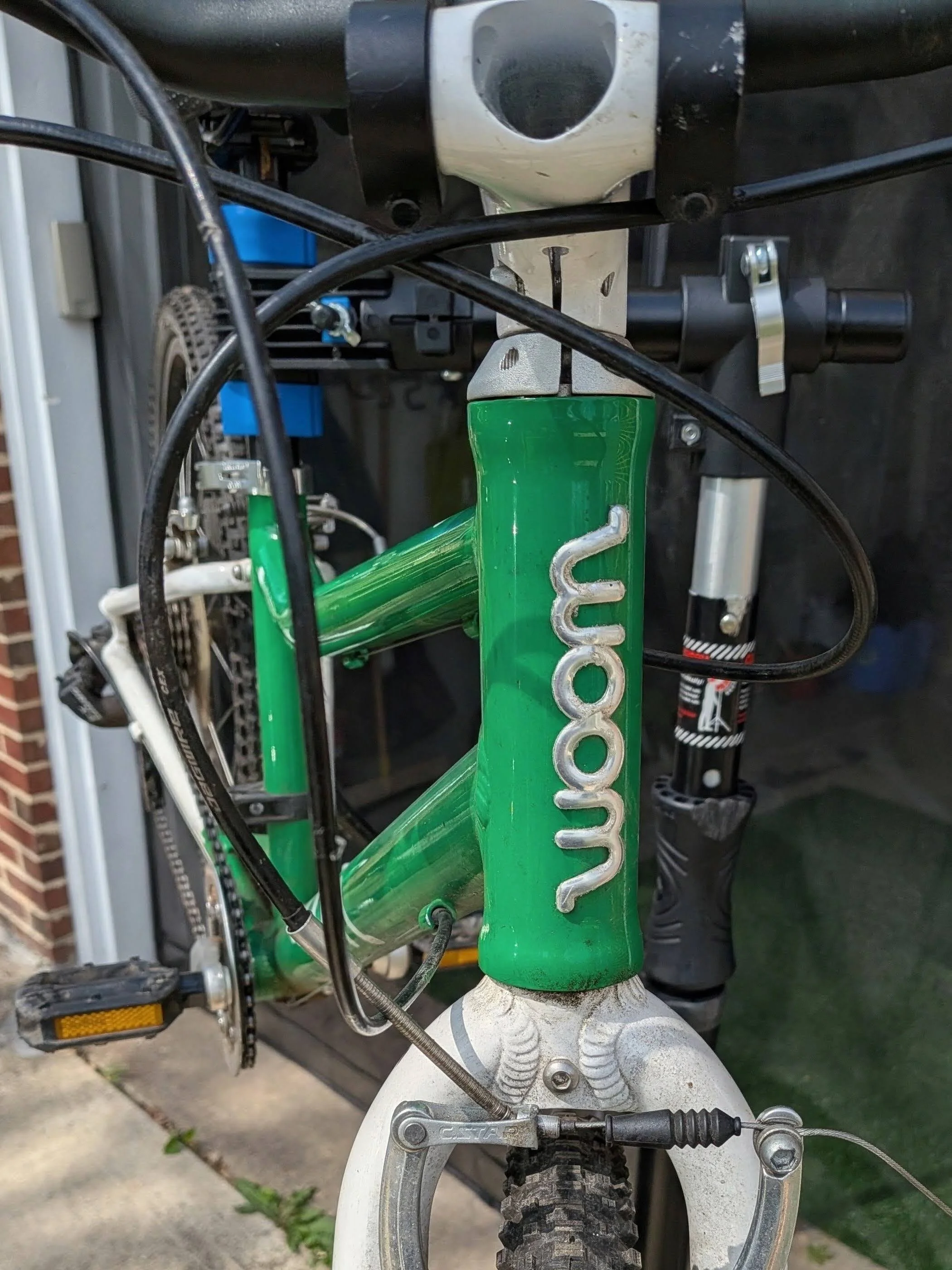 Close-up of a green front frame of a mountain bike, showing the head tube, front wheel, tire, and components like the brake and cable.