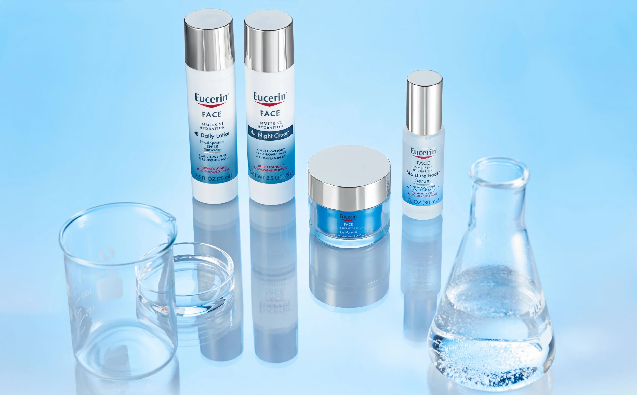 A collection of Eucerin skincare products including creams, serums, and lotions arranged on a reflective surface with clear laboratory glassware nearby.