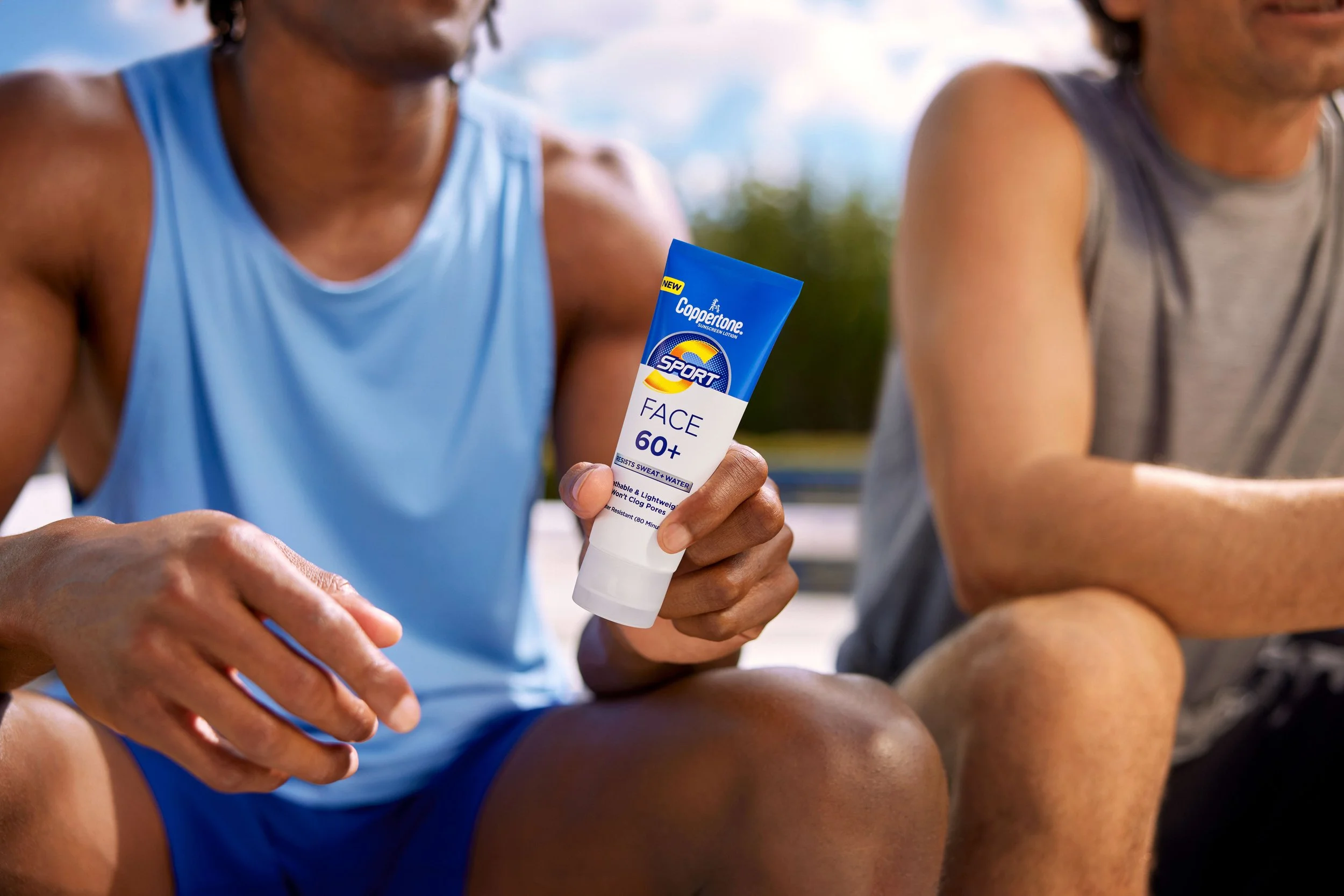 A person in a blue sports shirt applying Coppertone Sport sunscreen lotion to their arm during outdoor activity.