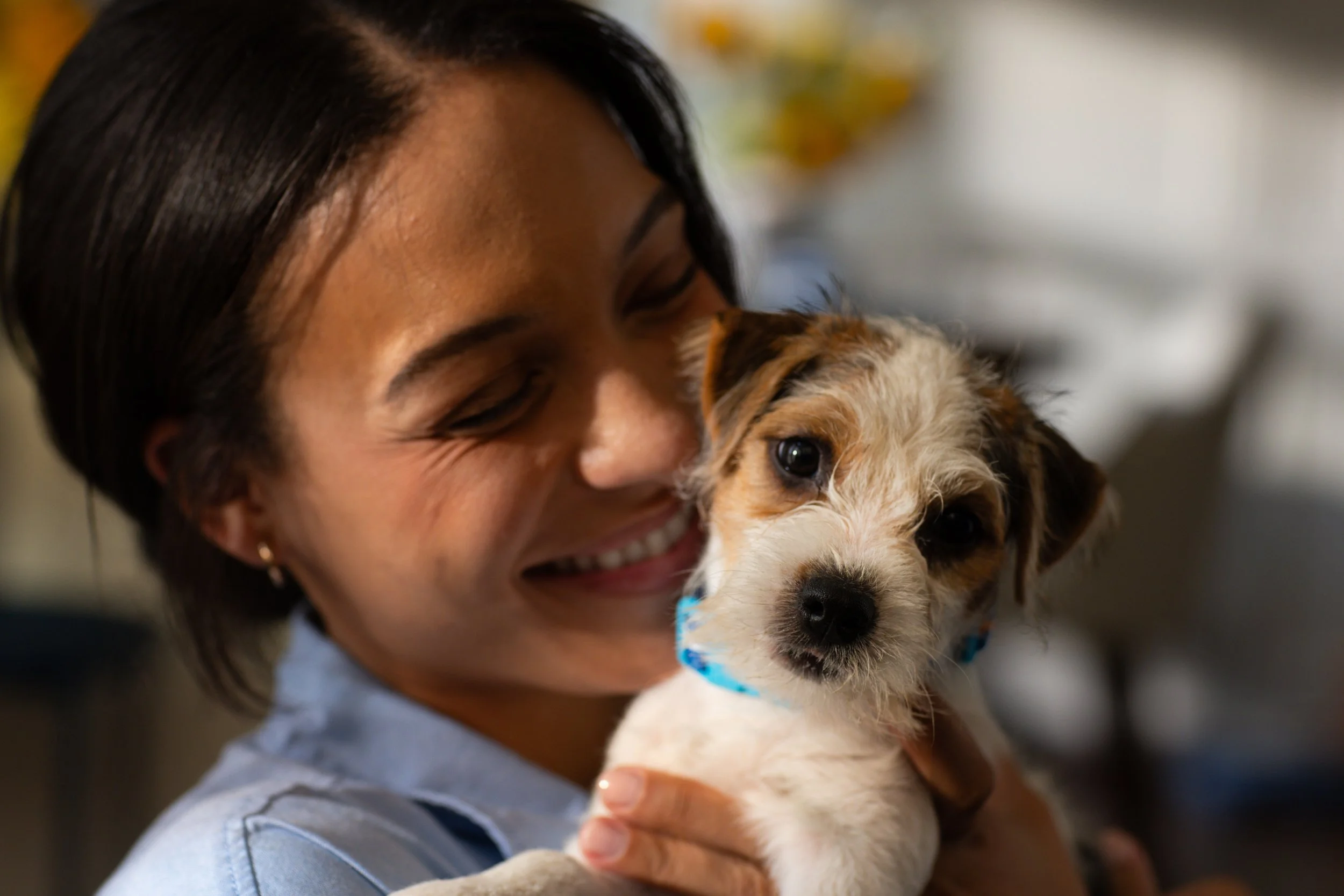 A woman with dark hair smiling and holding a small puppy with brown and white fur.