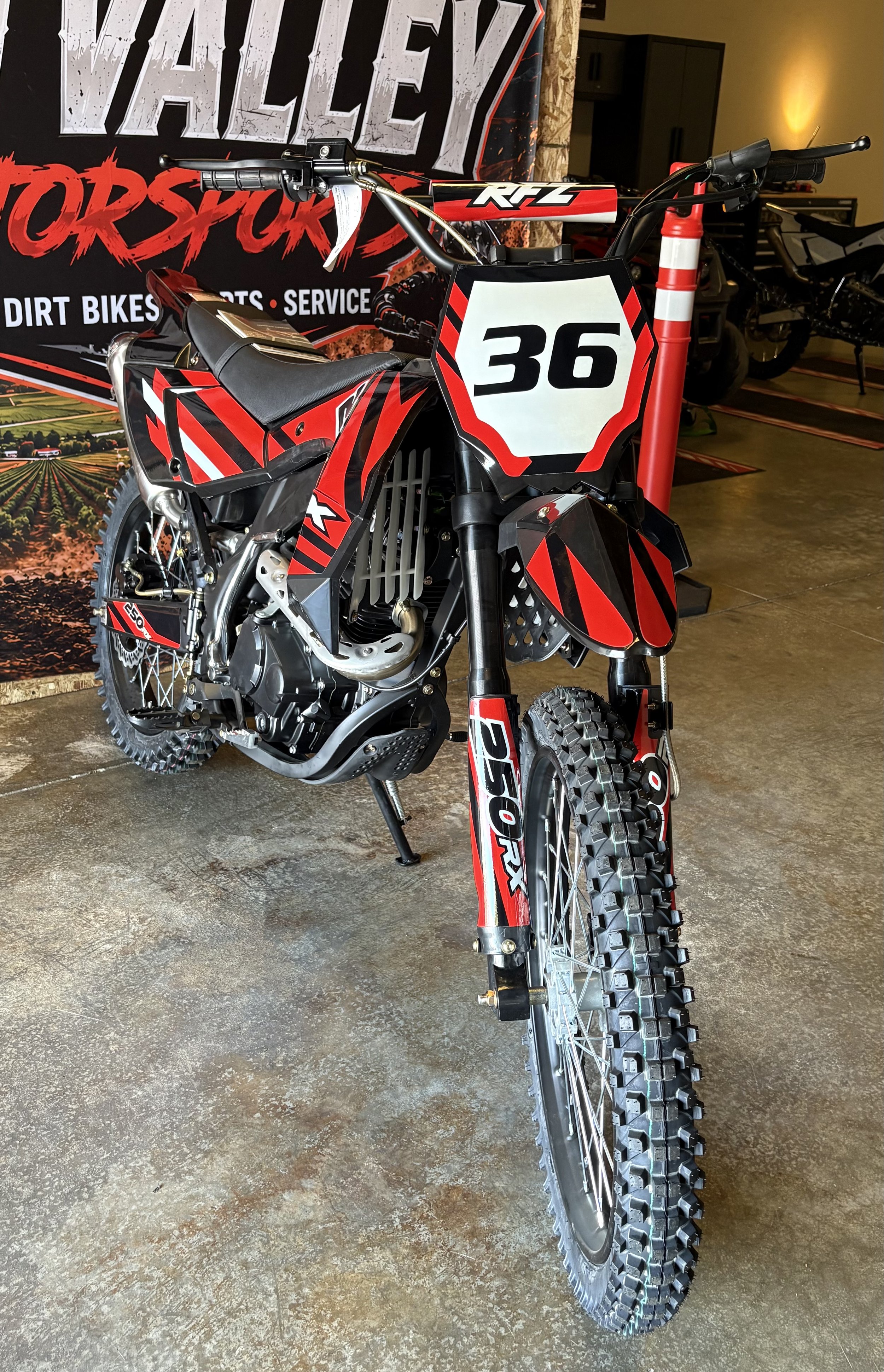 A dirt bike with red, black, and white graphics, the number 36 on the front, and knobby tires, displayed indoors at a motorsports shop.