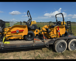Two yellow lawn seeding machines on a trailer in an open field.