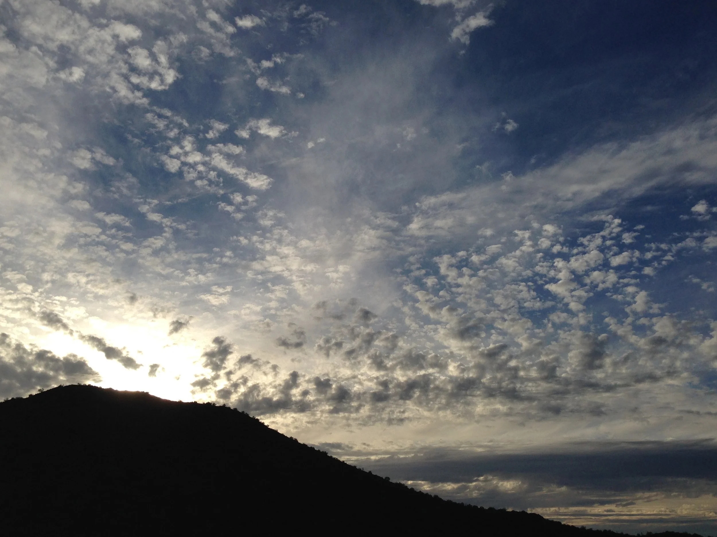Sky with scattered clouds over a silhouetted hillside at sunset or sunrise.