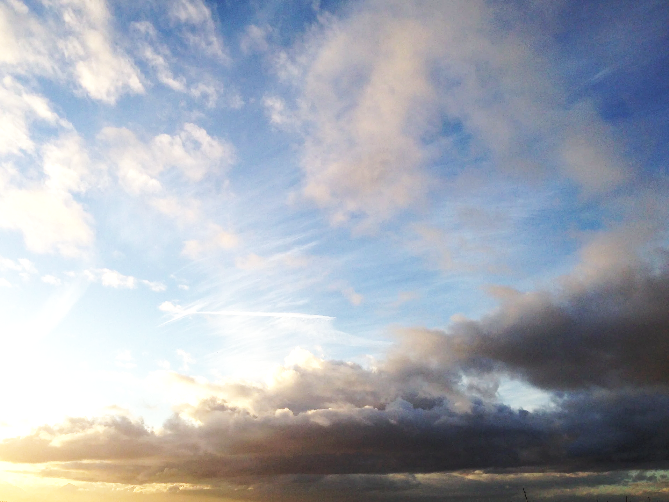 A partly cloudy sky during sunset or sunrise with various shades of blue and some fluffy clouds.