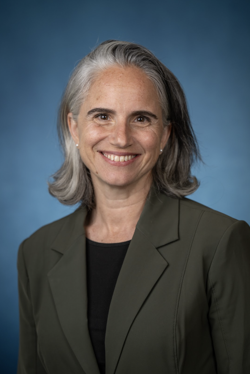 A mature woman with silver hair, smiling, wearing a dark green blazer over a black top, against a blue background.