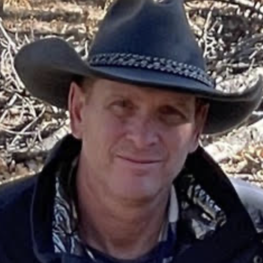 A man wearing a cowboy hat outdoors, with a background of dry branches or twigs.
