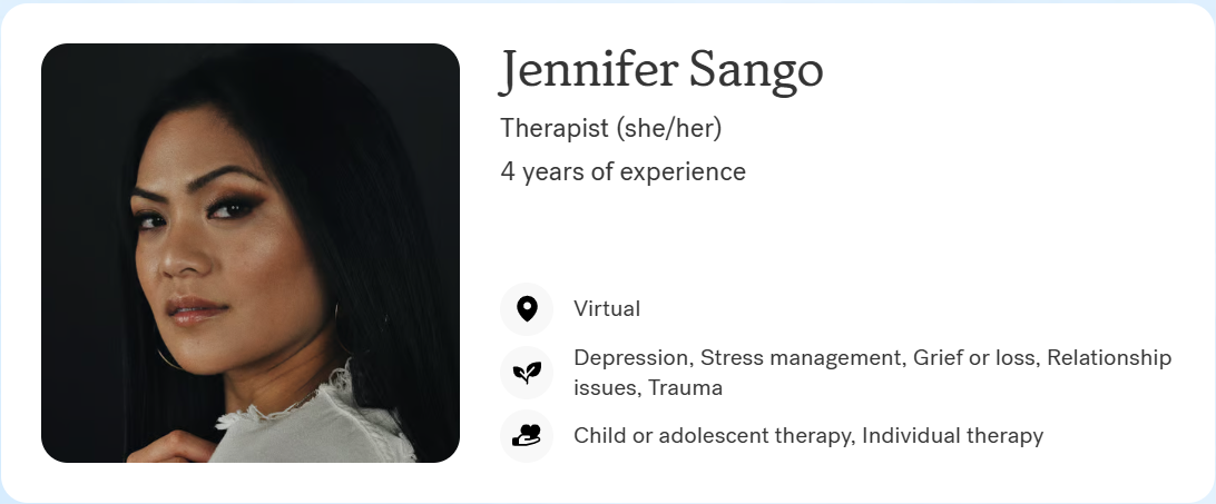 Portrait of Jennifer Sango, a therapist with long dark hair, wearing a white top, and looking at the camera against a dark background.