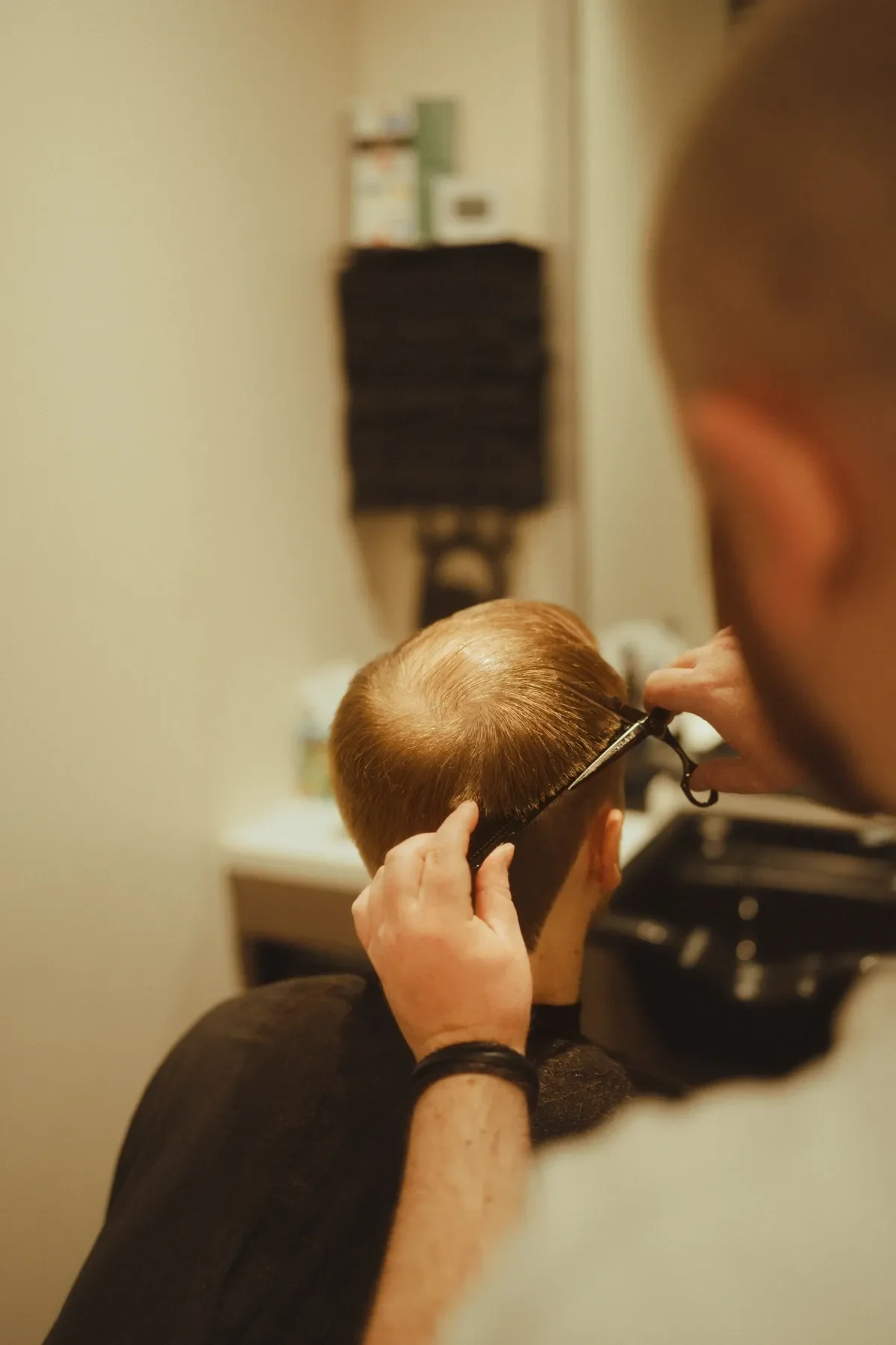 A person getting a haircut, with the barber using scissors to trim the person's short, light brown hair.