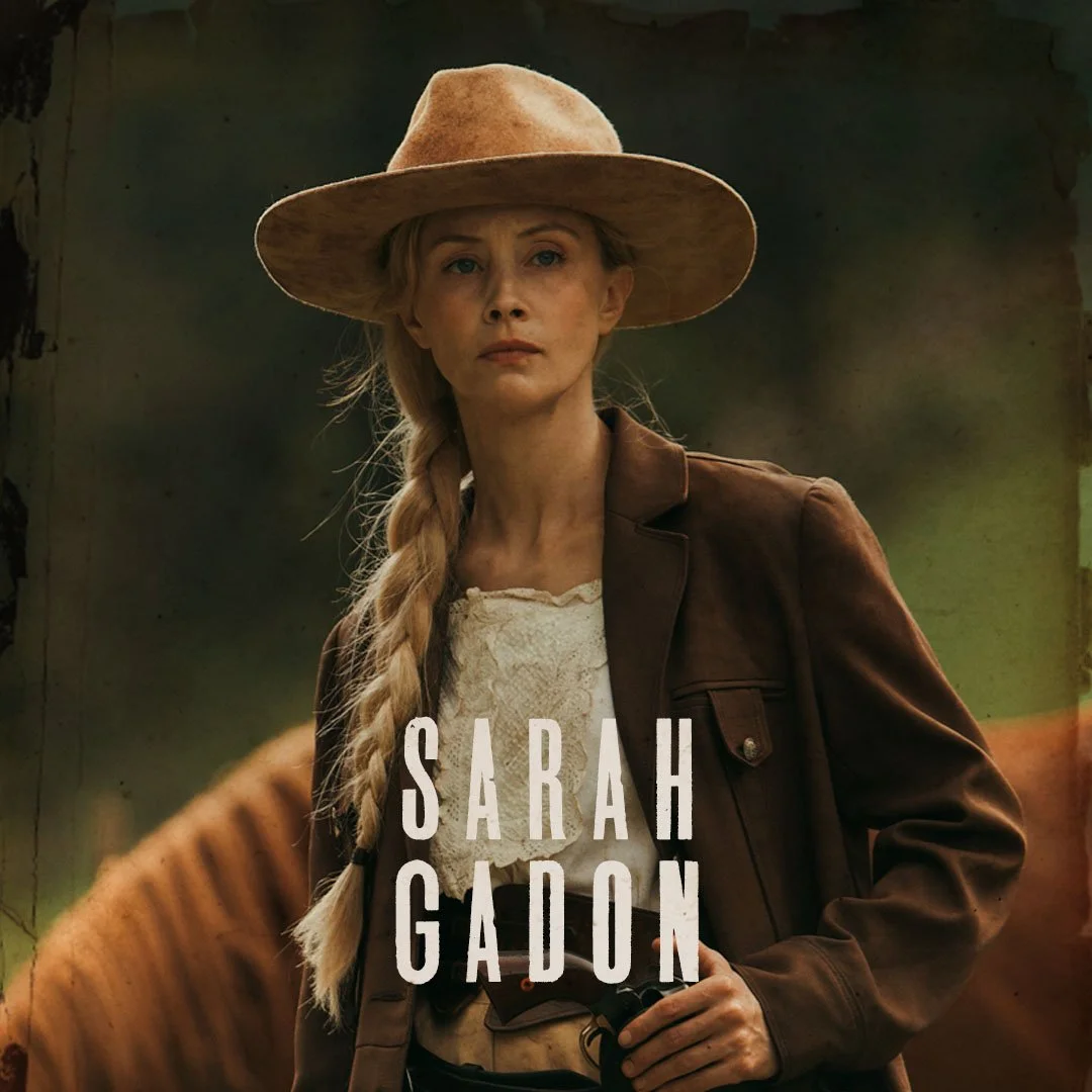 A woman dressed as a cowboy, wearing a wide-brimmed hat, a brown leather jacket, and holding a gun, standing outdoors with a blurred background. The text 'Sarah Gadon' is overlaid on the image.