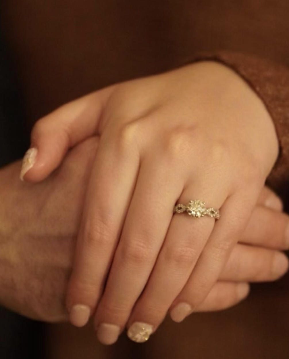 Close-up of a woman's left hand resting on her lap, showing a gold ring with a central gemstone on her ring finger.