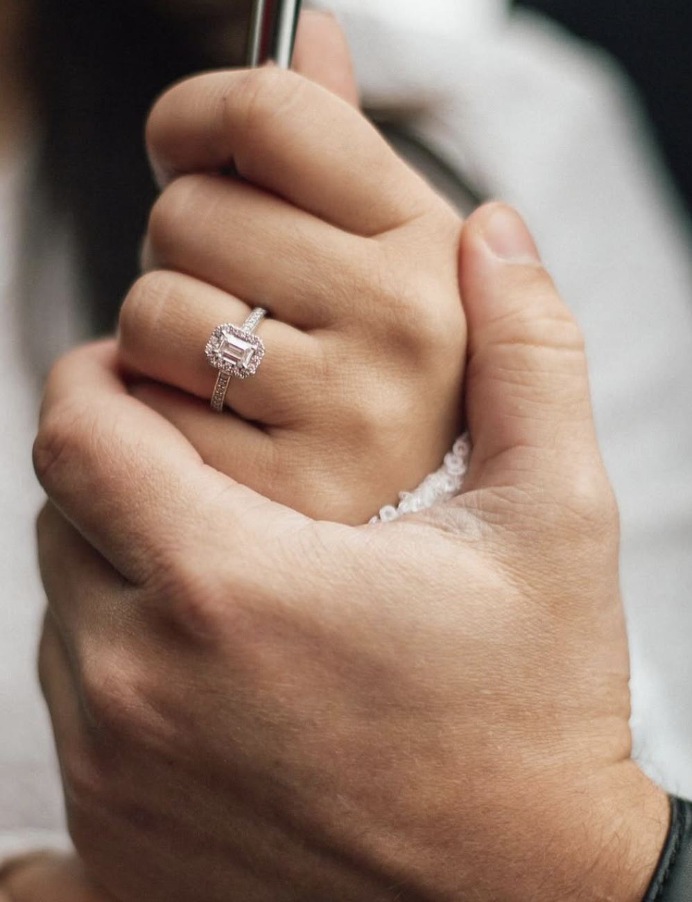 Close-up of a hand with a diamond ring on finger, gently holding another person's hand.