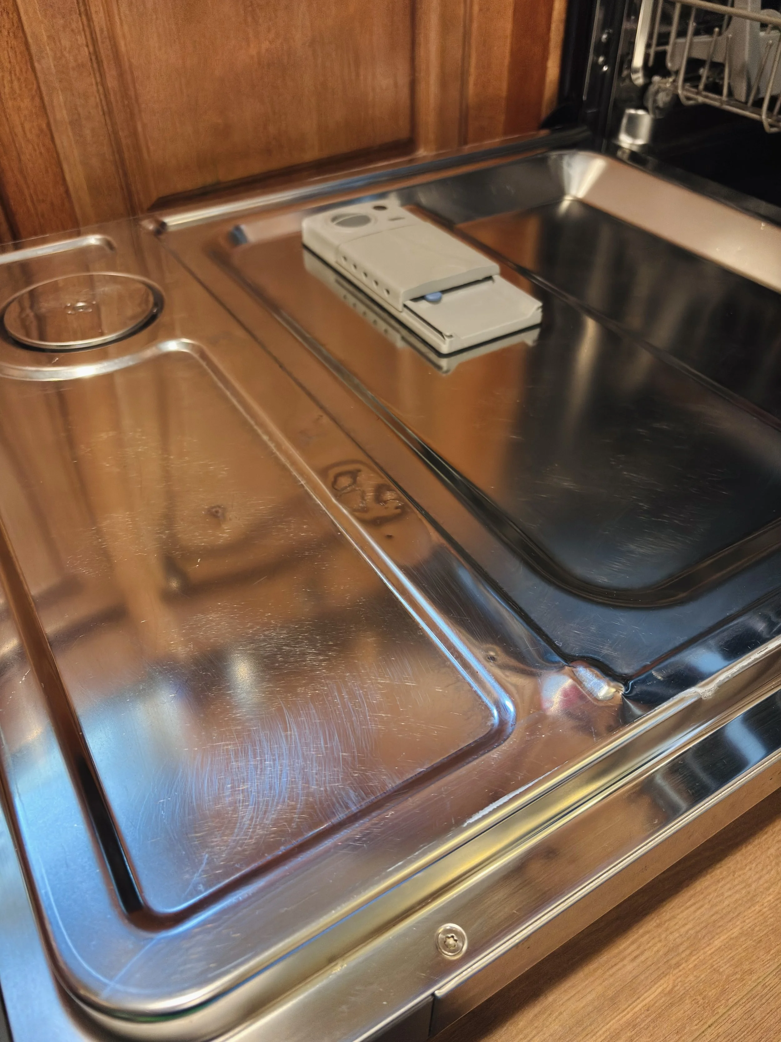 A stainless steel kitchen sink with a soap dispenser and a drip tray, with a wooden wall background.