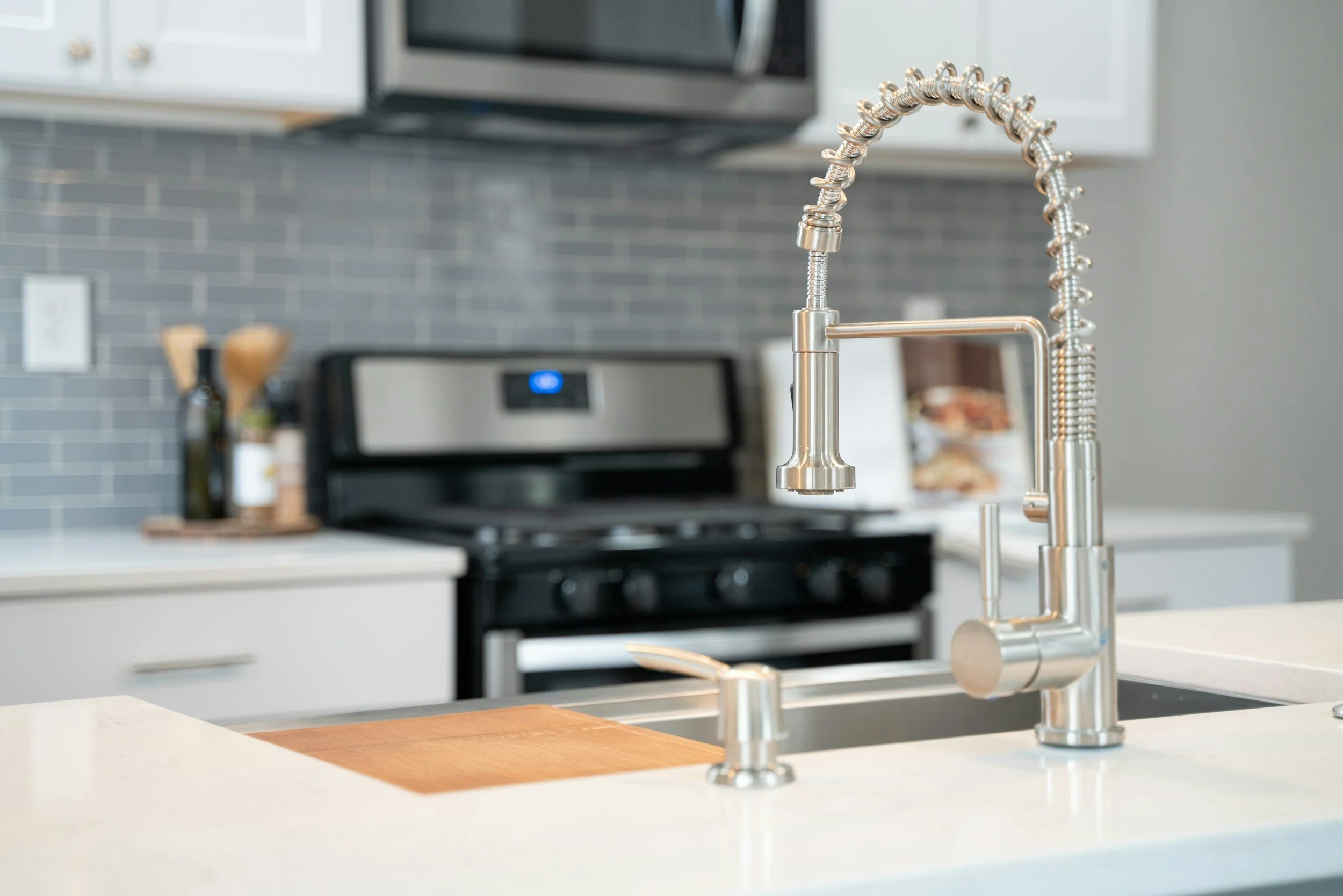 Modern kitchen with stainless steel faucet and soap dispenser, black stove, gray subway tile backsplash, and white cabinets.