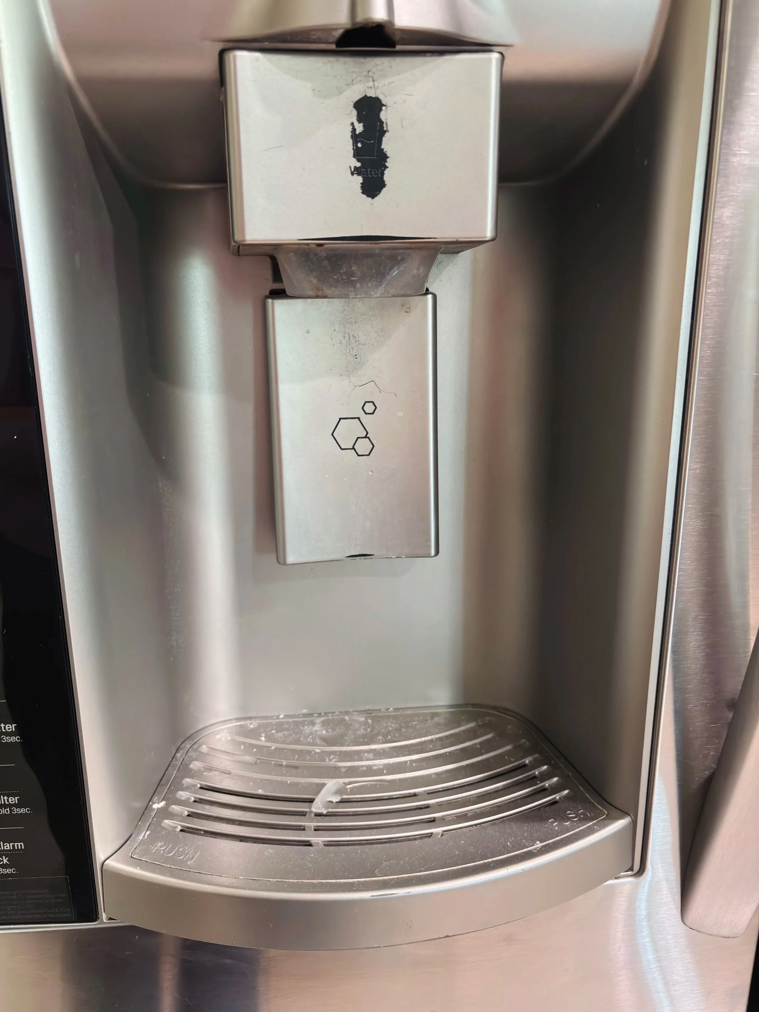 Close-up of a stainless steel water dispenser with a lever and a drip tray at the bottom.