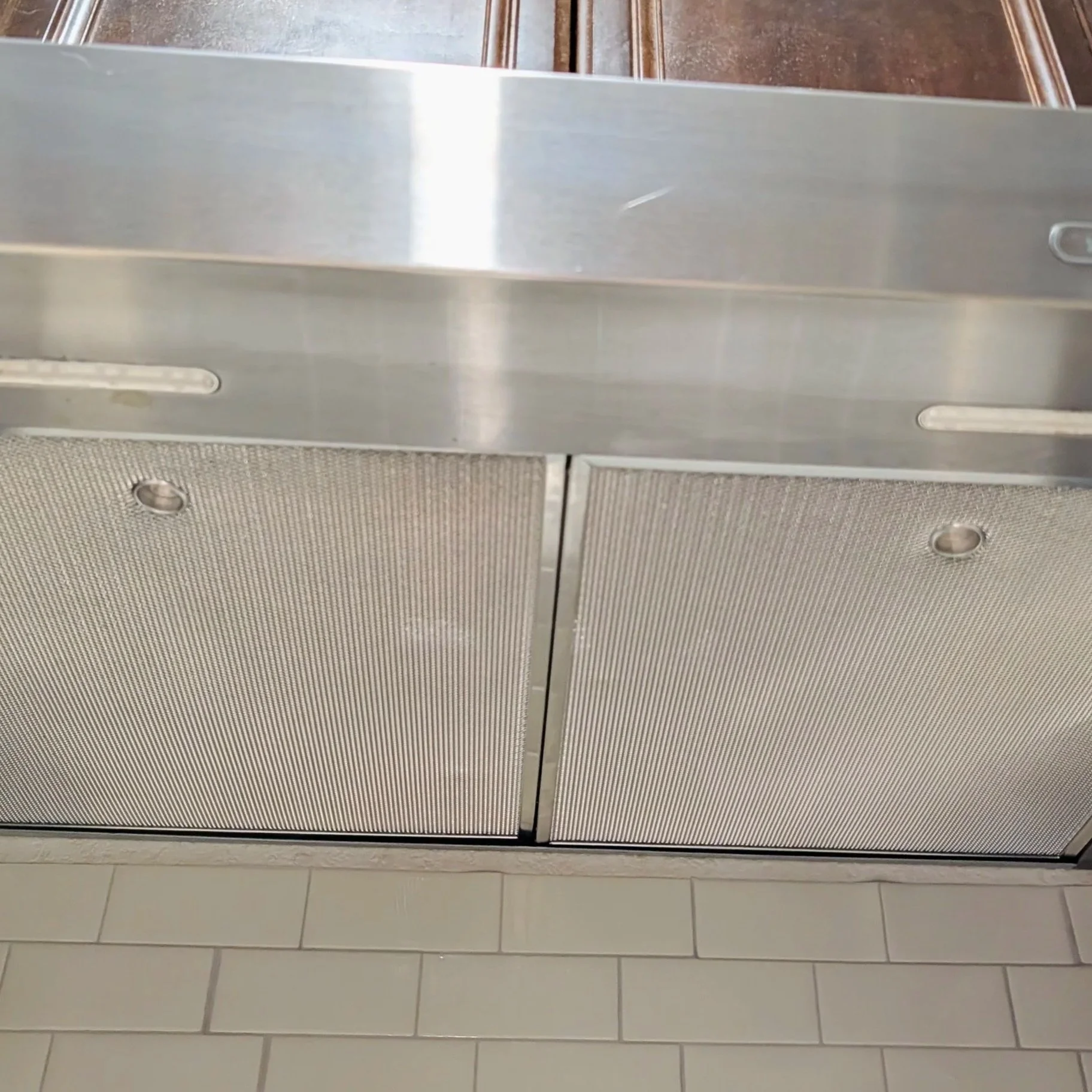 A stainless steel commercial dishwasher with two doors, situated above beige tiled flooring.