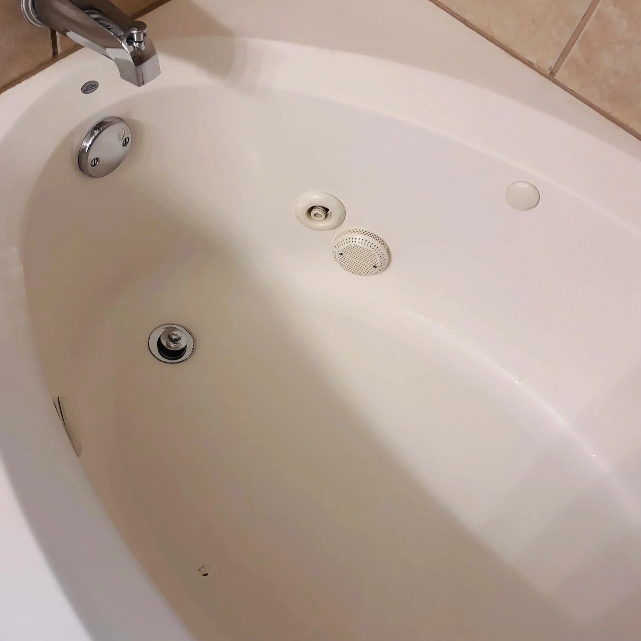 A white bathtub with a silver faucet and drain, surrounded by beige tiled walls.