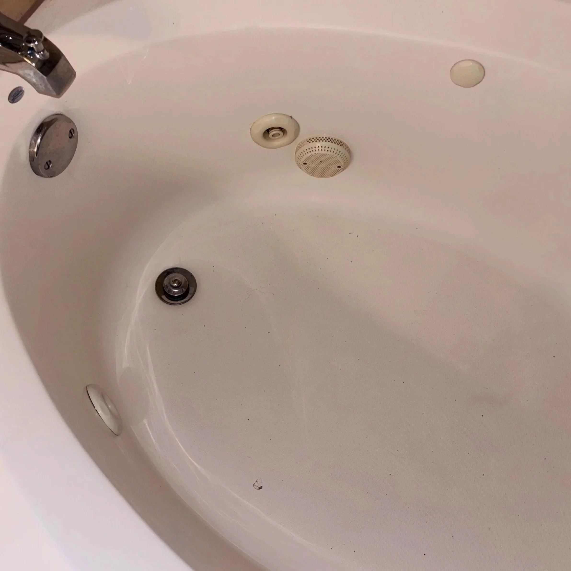 Close-up of the interior of a white bathtub showing a drain, two jets, and a small circular soap holder, with a chrome faucet visible on the left.