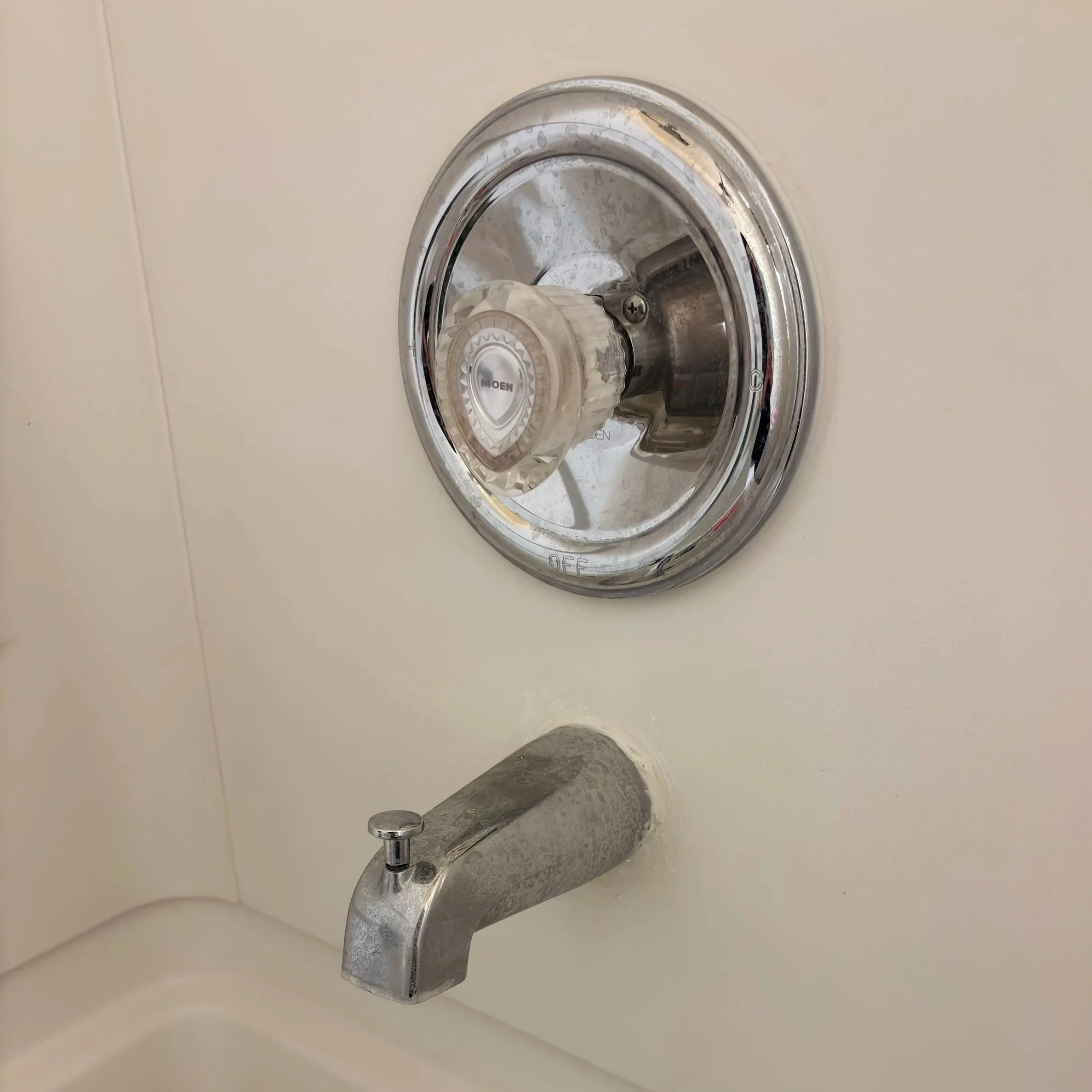 Close-up of a bathroom sink faucet with the water turned off, mounted on a white wall.