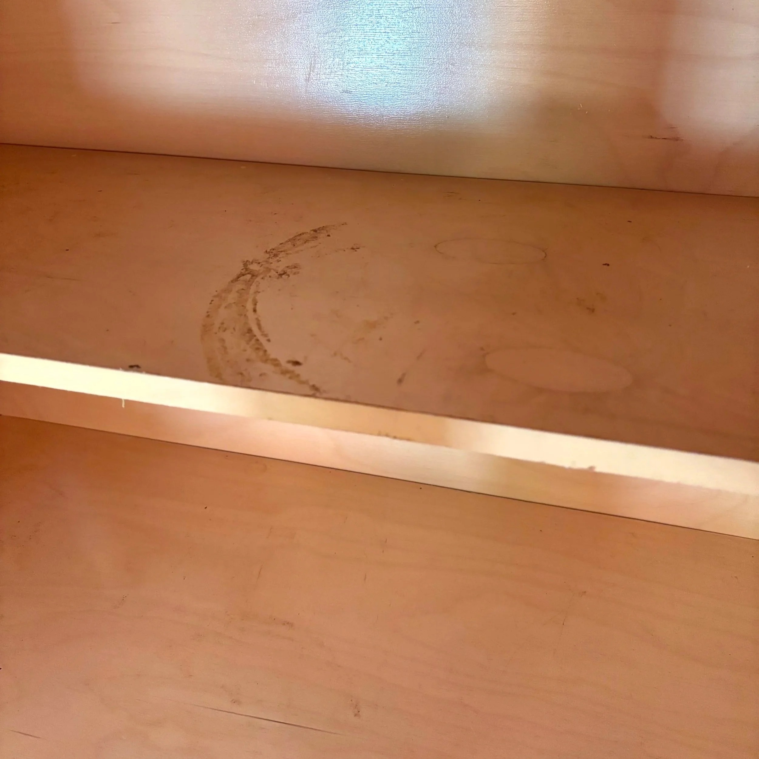 A close-up photo of the bottom of a wooden piece of furniture with visible scratches and marks.