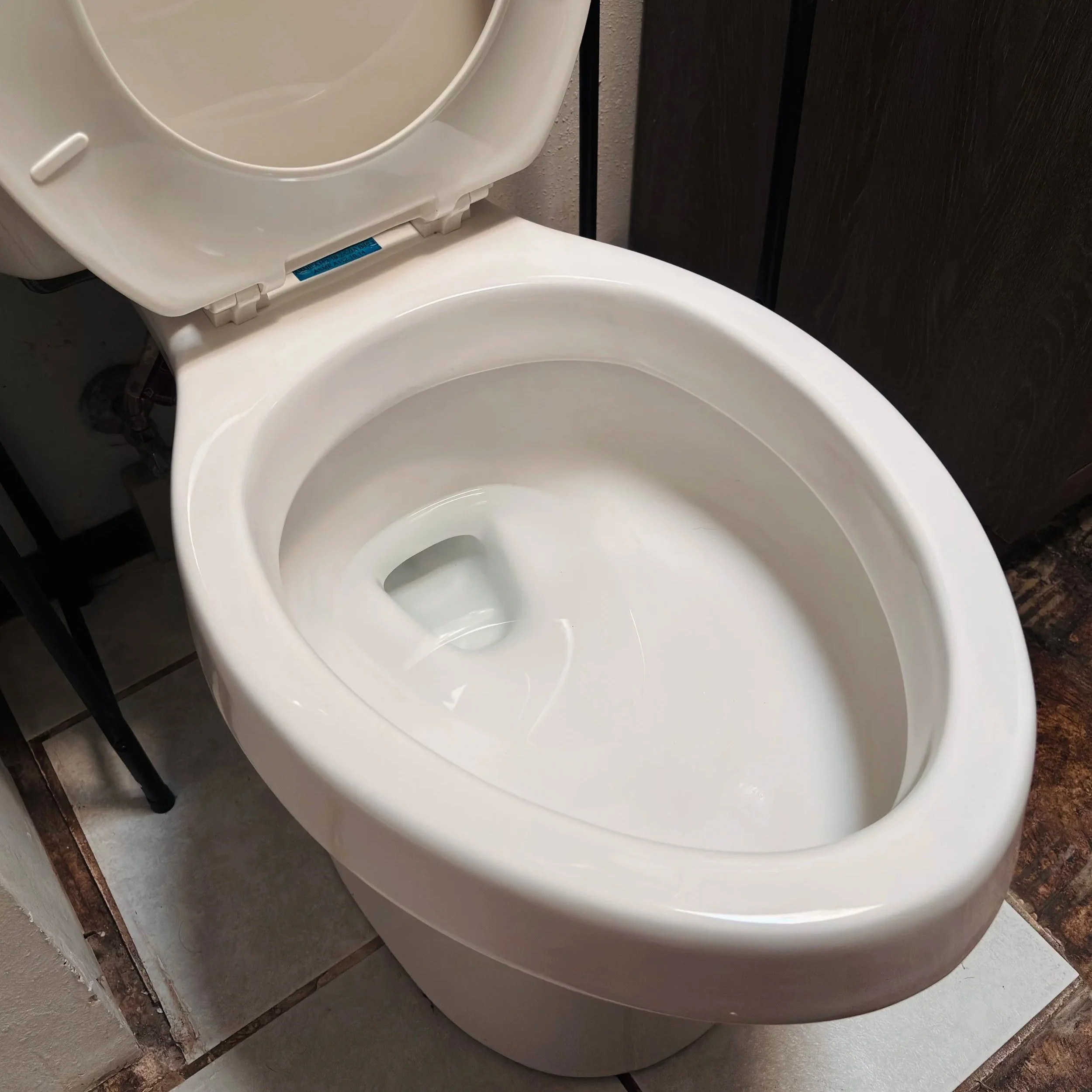 A white porcelain toilet with the lid open, placed against a wall with dark brown paneling.