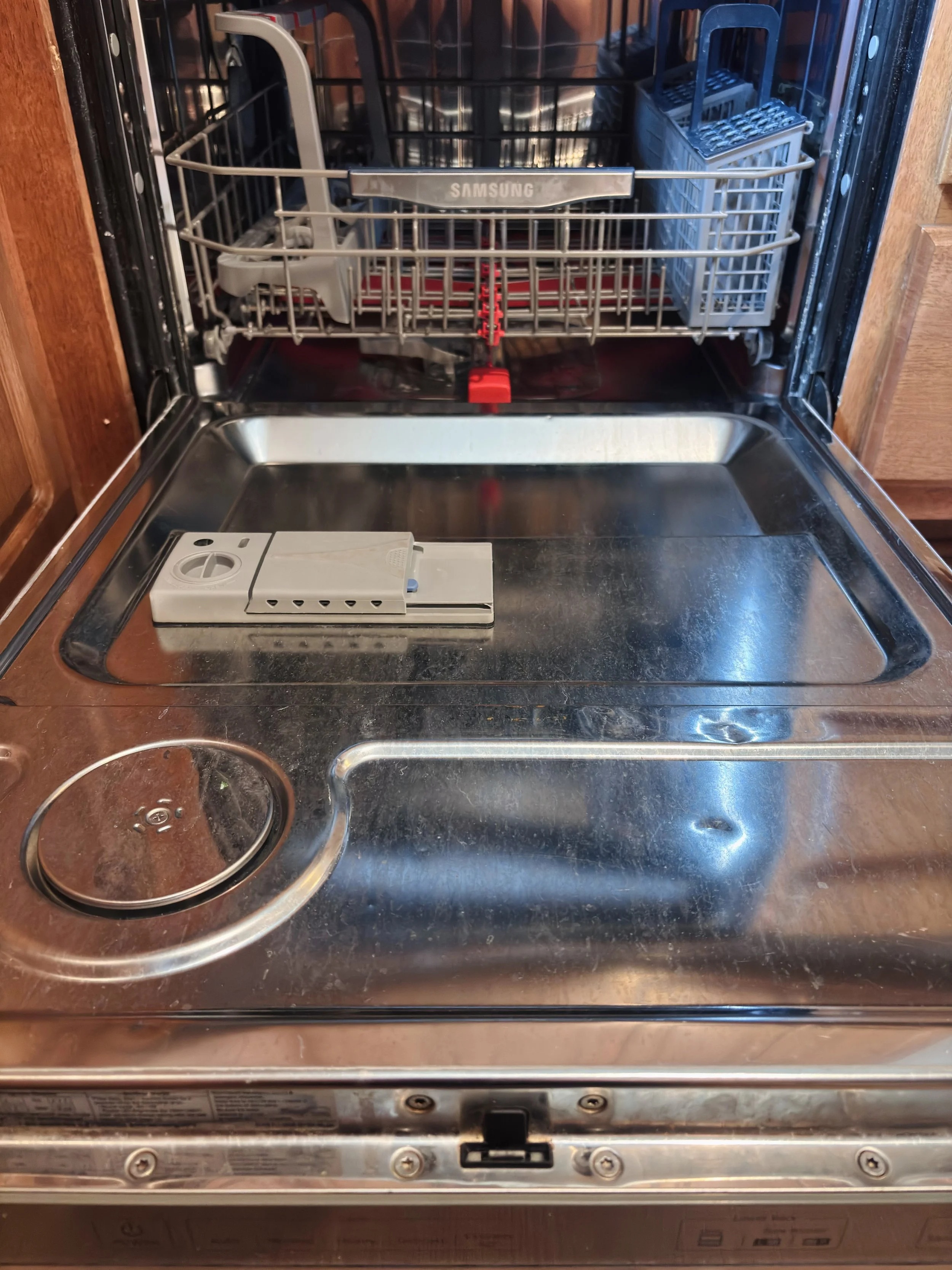 Open dishwasher with empty racks and a metal tray on the lower left corner